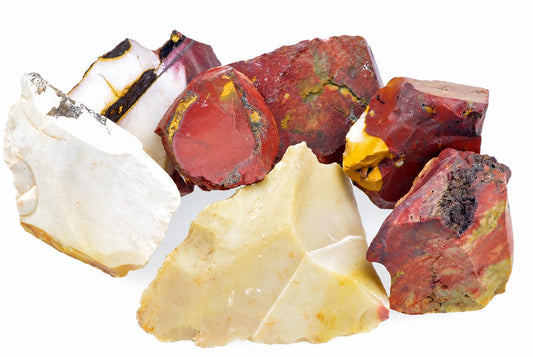 A collection of raw Mookaite jasper pieces in red, white, yellow and black on a pale surface.