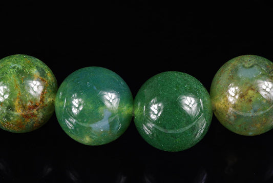 Four round green beads with yellow and brown inclusions on a dark surface.