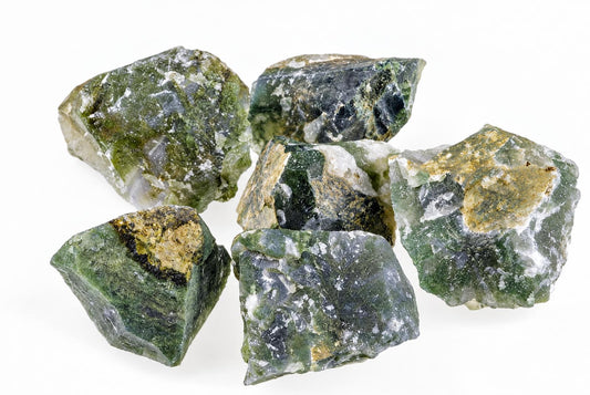 Six rough moss agate stones with green, white and brown patches on a pale surface.