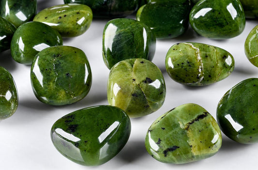 Several polished green stones with black speckles and some white veins lie on a pale surface.
