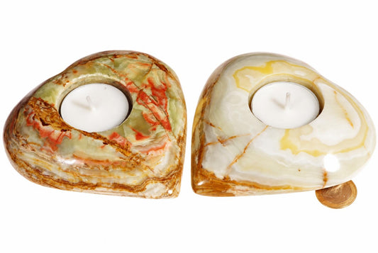 Two heart-shaped onyx candle holders with white tea lights, one green-red and one cream-yellow, on a pale surface.