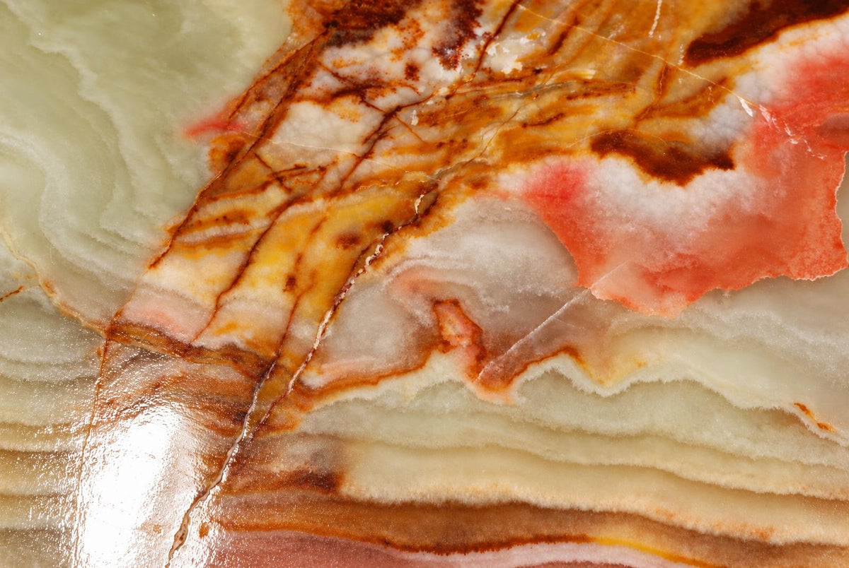 A polished stone slab with swirling bands of pale green, white, brown and pink on a dark surface.
