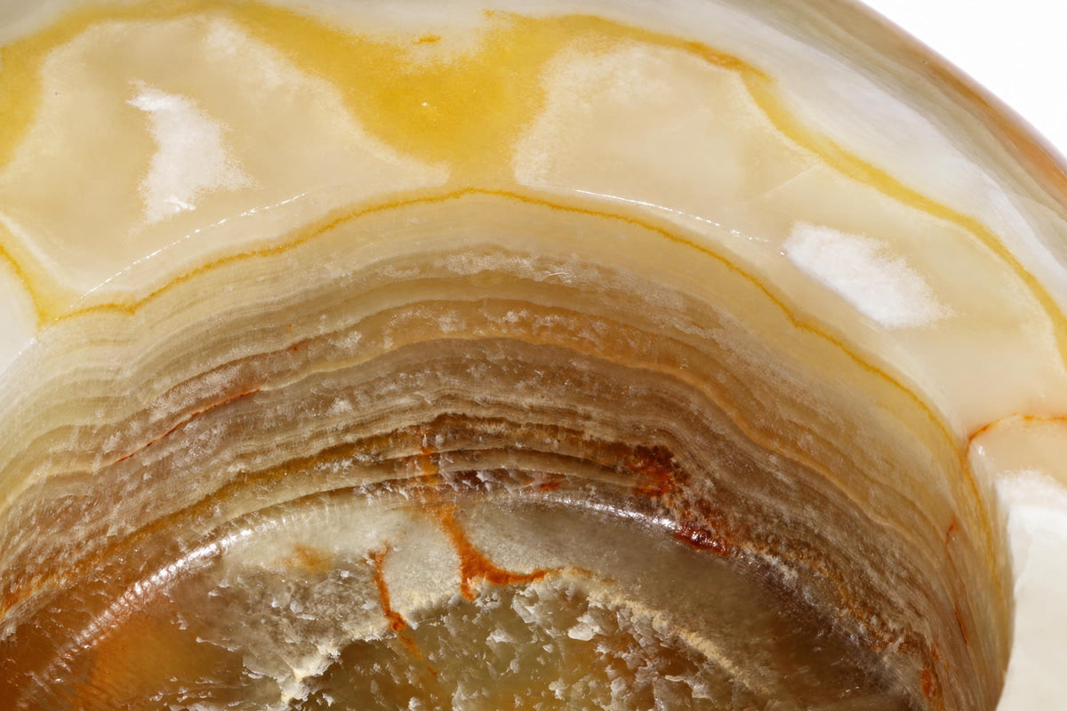 A polished onyx bowl with curved, layered bands of cream, yellow, and brown minerals.