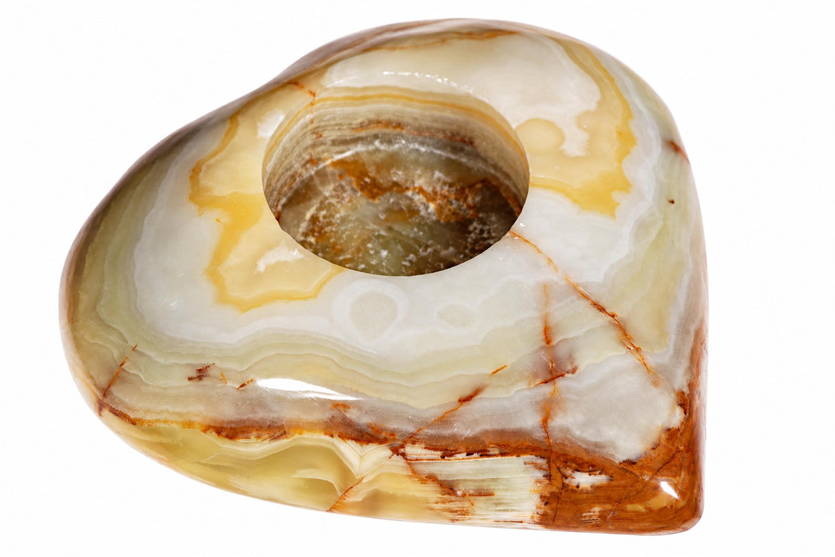 A polished, heart-shaped onyx candle holder with a central hole. It features swirling bands of white, cream, yellow, and brown against a plain background.