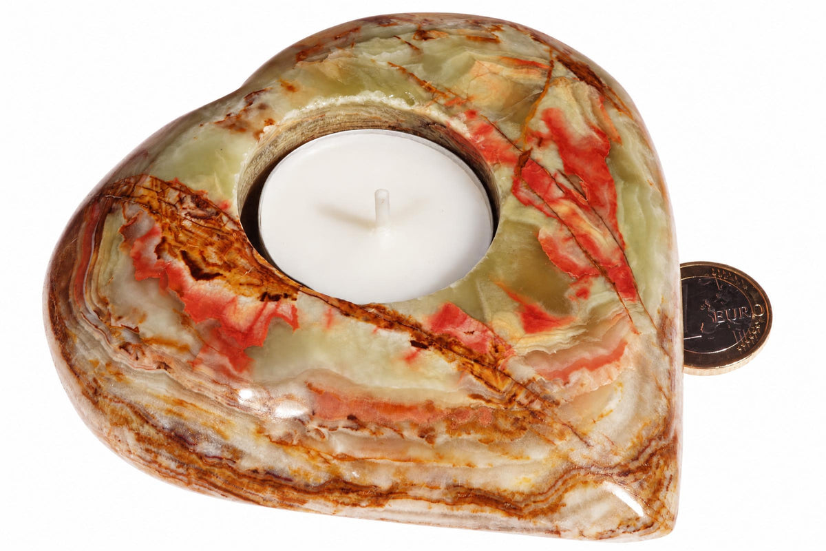 A heart-shaped candle holder made of polished stone with green, red and brown swirls holds a white tea light on a pale surface.