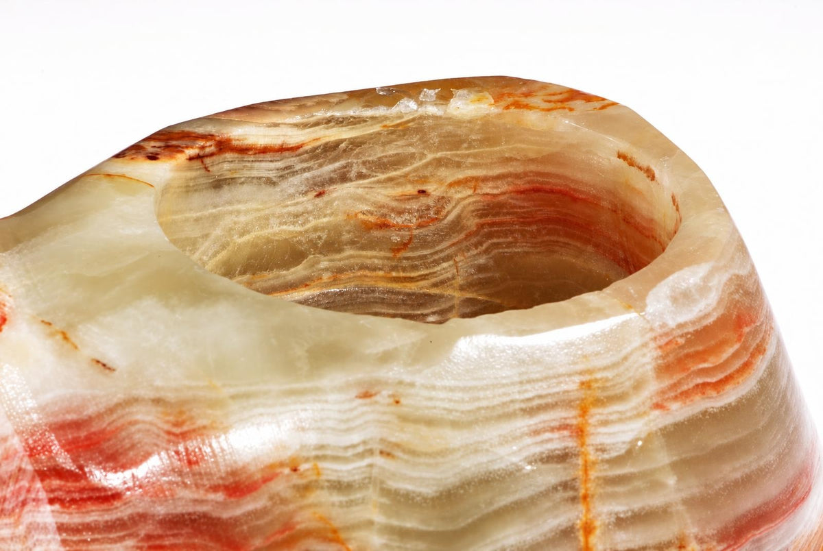 A polished onyx candle holder with a rounded bowl shape, featuring layered bands of cream, orange and brown against a white background.