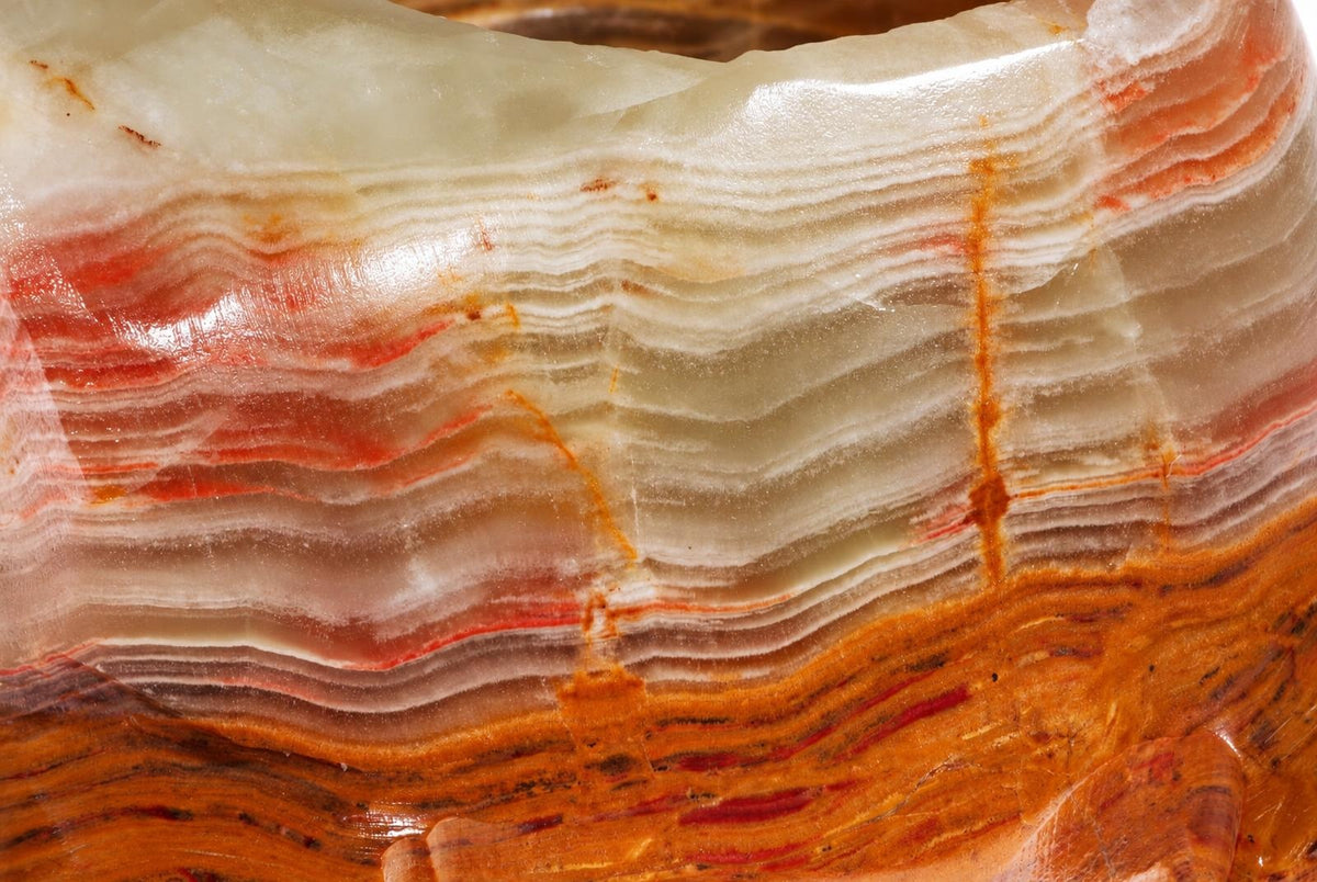 A polished stone object with wavy layers of white, red, orange and brown on a dark surface.