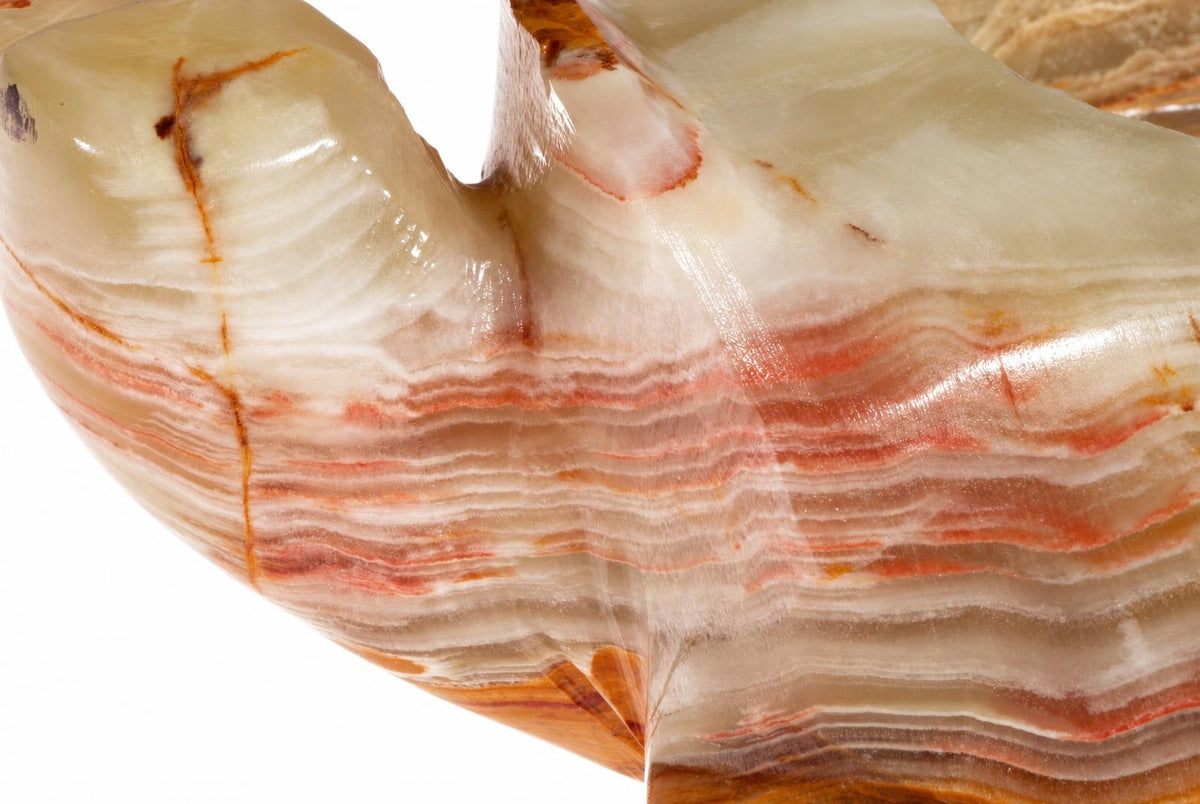 A polished, curved piece of layered onyx with white and reddish-brown bands against a pale surface.