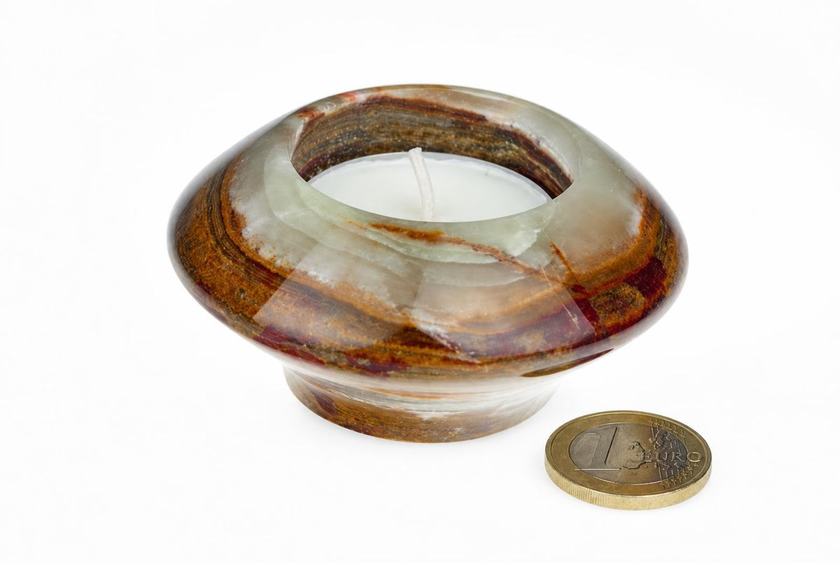 A polished, ring-shaped candle holder with brown and white banded stone holds a white tea light on a pale surface.
