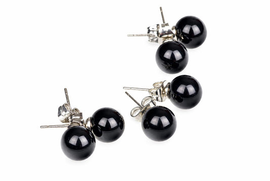 Two pairs of round black stud earrings with silver-toned posts and butterfly backs on a white surface.