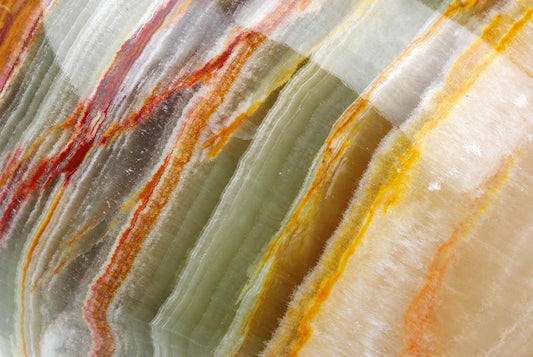 A polished slab of onyx displaying diagonal bands of pale green, white, and reddish-orange stripes.