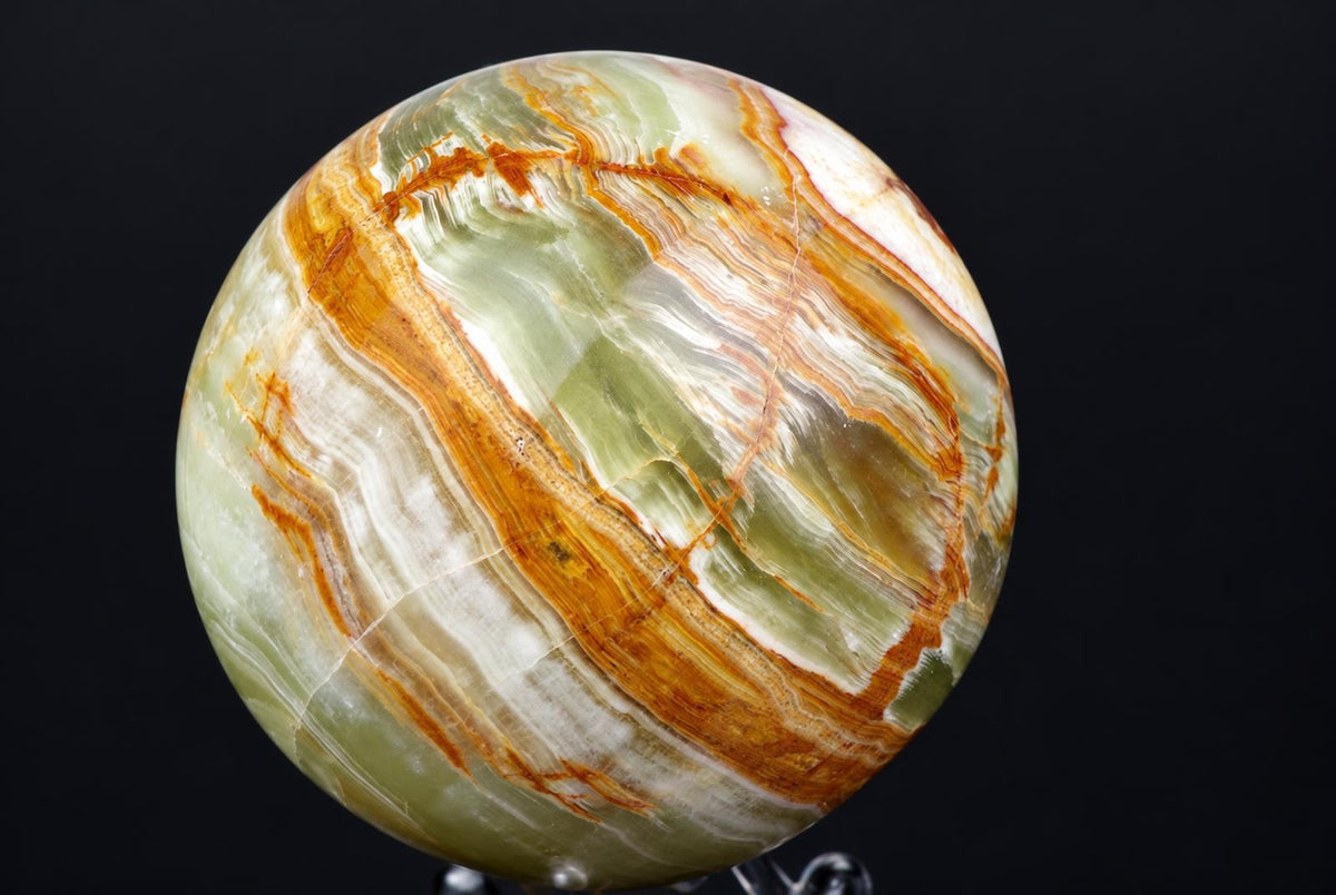 A polished sphere with green, white and orange-brown wavy bands on a dark surface.