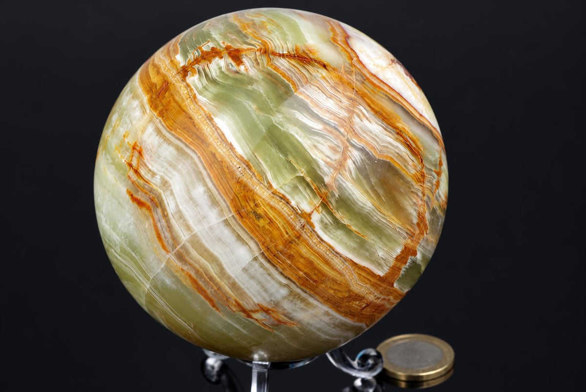 A polished, spherical stone with green, white and orange-brown banding sits on a clear stand against a dark background.