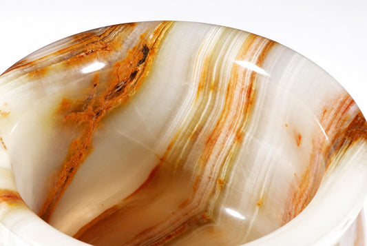 A polished onyx bowl with swirling white, cream, and brown stripes viewed from above against a pale surface.