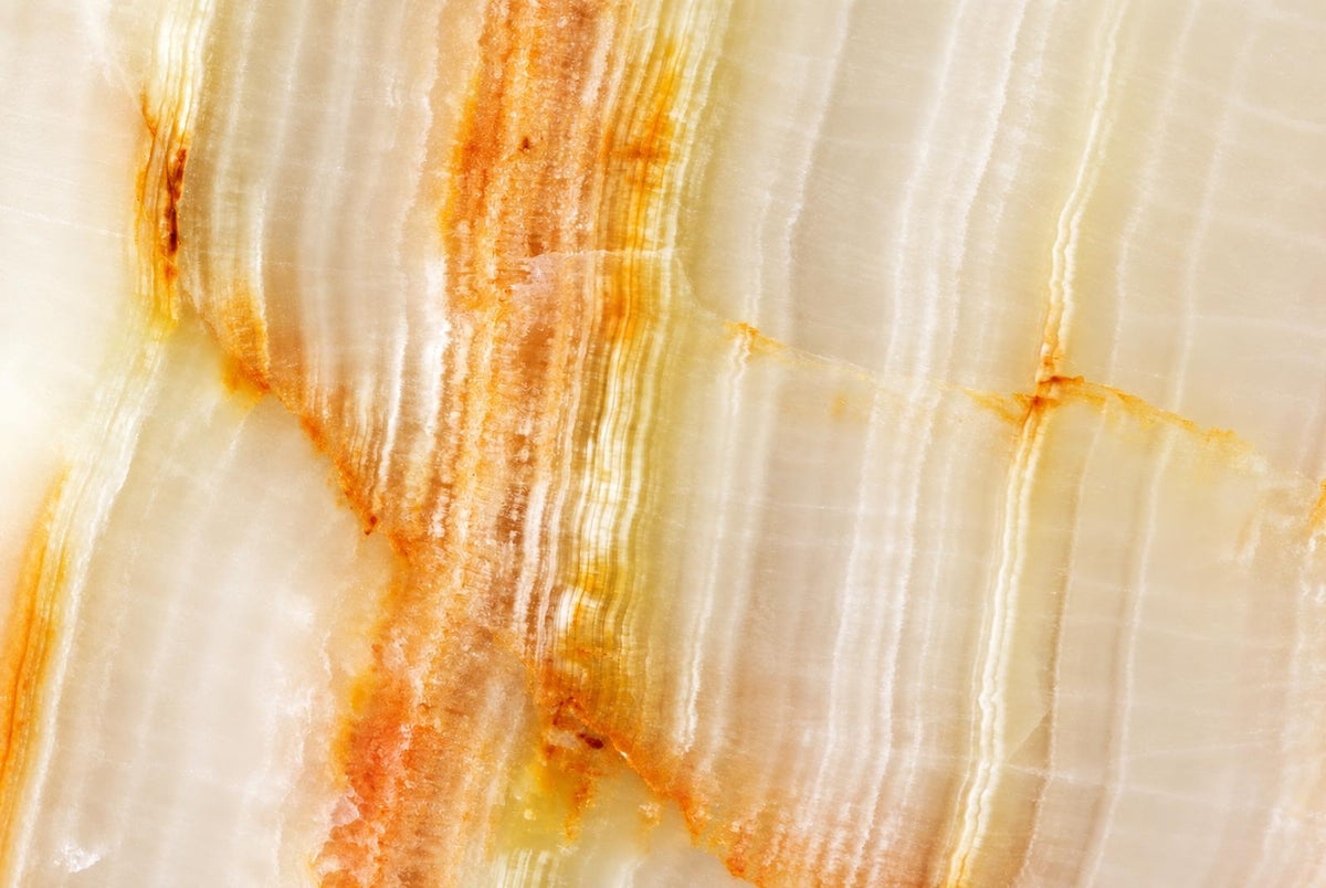 A close-up of a polished stone surface with white and pale yellow layers, featuring orange-brown veining.