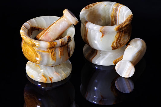 Two pale stone mortars with brown and gold-colored bands are displayed with matching pestles on a reflective black surface.