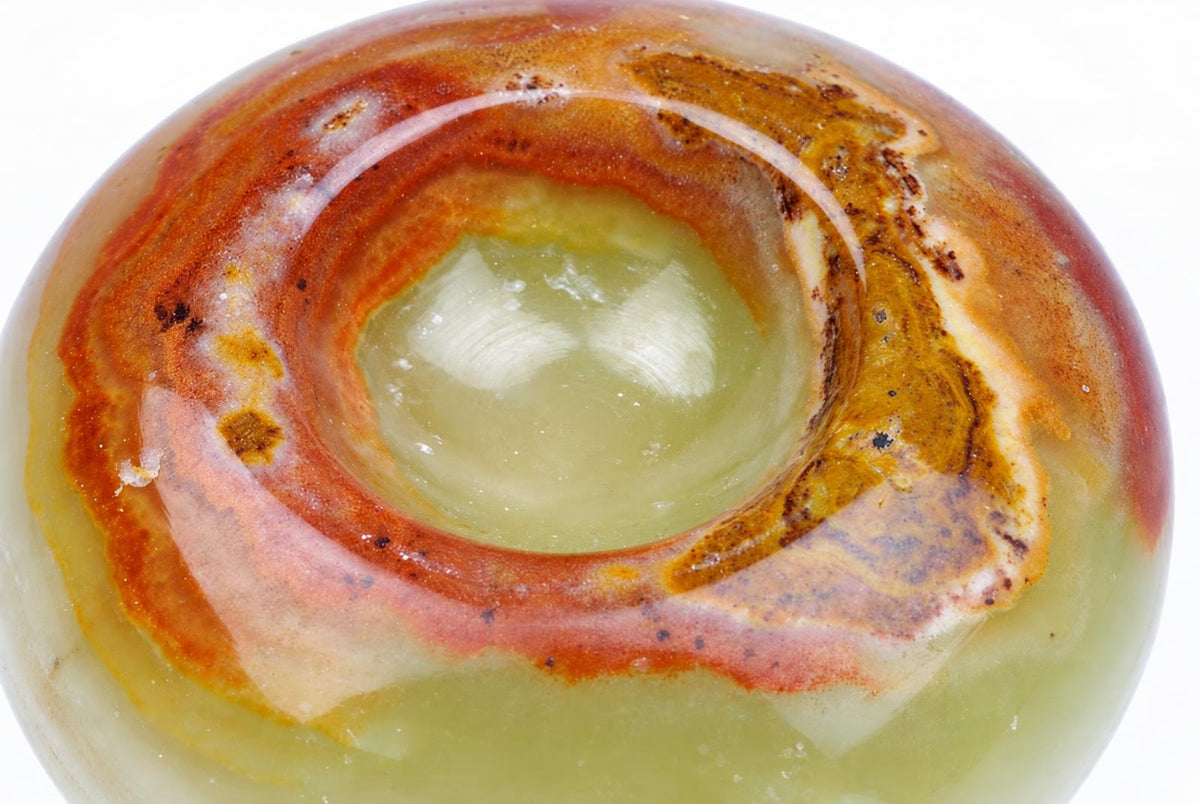 A polished onyx stand top with concentric bands of green, orange, red and brown against a white background.