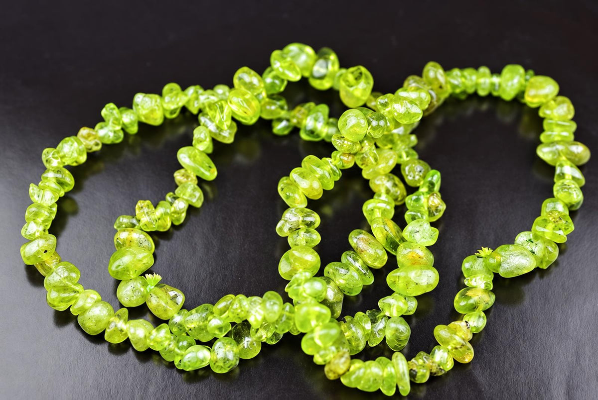A strand of bright green peridot chip beads arranged in a loose coil on a dark surface.