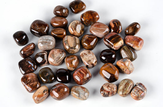 A pile of polished, tumbled stones with brown, tan and grey banding on a white surface.