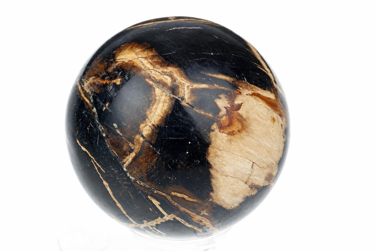 A polished stone sphere with black, tan and brown patches is displayed against a white background.