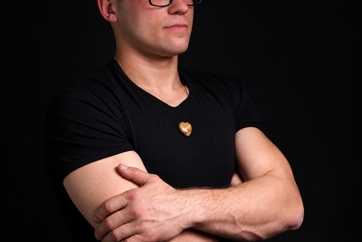 A man in a black t-shirt wears a heart-shaped pendant with brown and cream swirls on a dark surface.