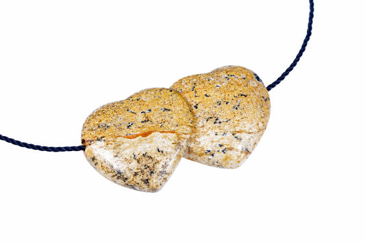 A pendant with two heart-shaped jasper stones in cream, yellow and black speckles on a dark blue cord against a white background.
