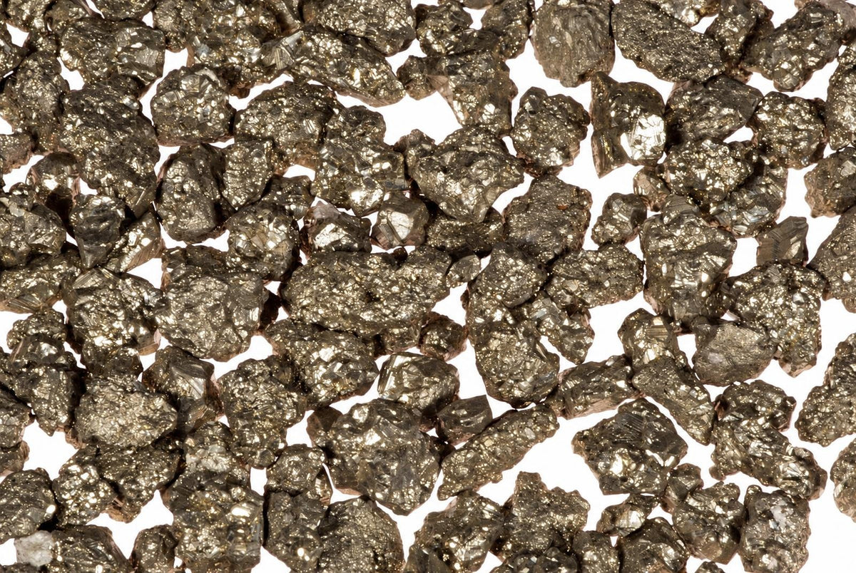 A pile of small, metallic, gold-coloured pyrite crystals scattered on a white surface.