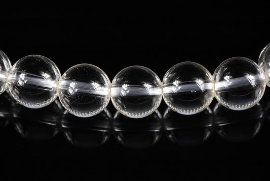 A row of clear, round quartz beads with internal inclusions on a dark reflective surface.