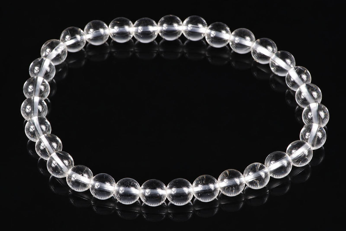 A bracelet of clear, round quartz beads on a dark reflective surface.