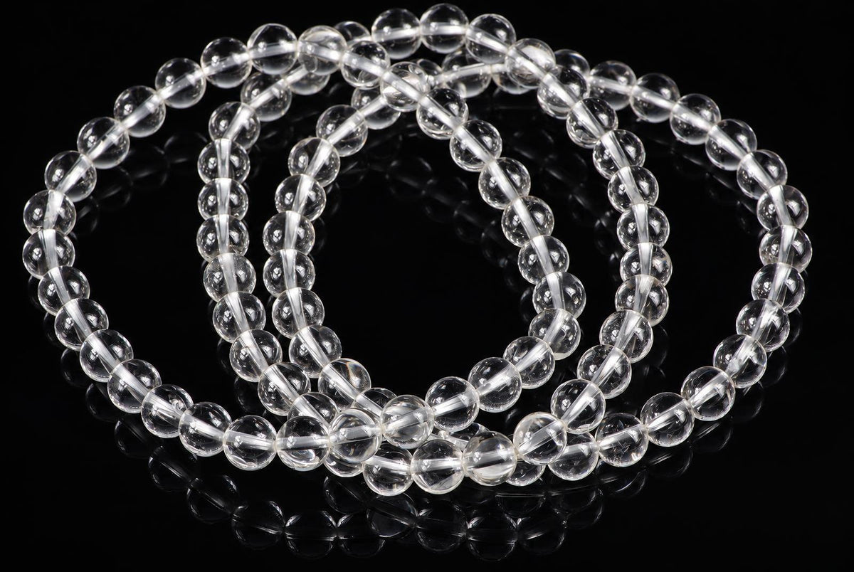 A clear quartz bracelet with round beads arranged in a loop on a dark reflective surface.