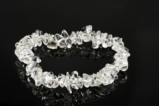 A bracelet made of clear, irregular quartz chips arranged in a circle on a dark reflective surface.