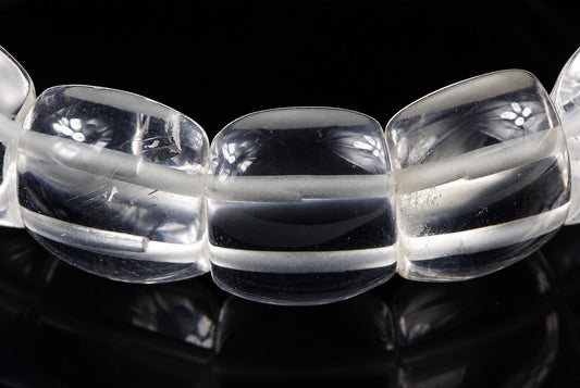 A close-up of a bracelet with large, clear quartz beads featuring frosted horizontal bands, set against a dark surface.