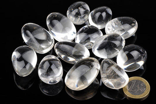 Twelve clear quartz stones on a dark surface with a one euro coin for scale.