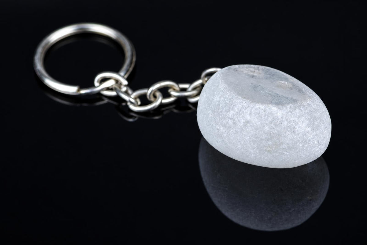 A silver-toned keychain with a smooth, white stone pendant rests on a dark, reflective surface.