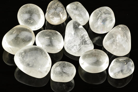 A group of smooth, clear quartz stones arranged on a dark surface.