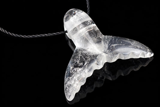 A clear quartz pendant shaped like a dolphin tail hangs from a dark cord against a black background.