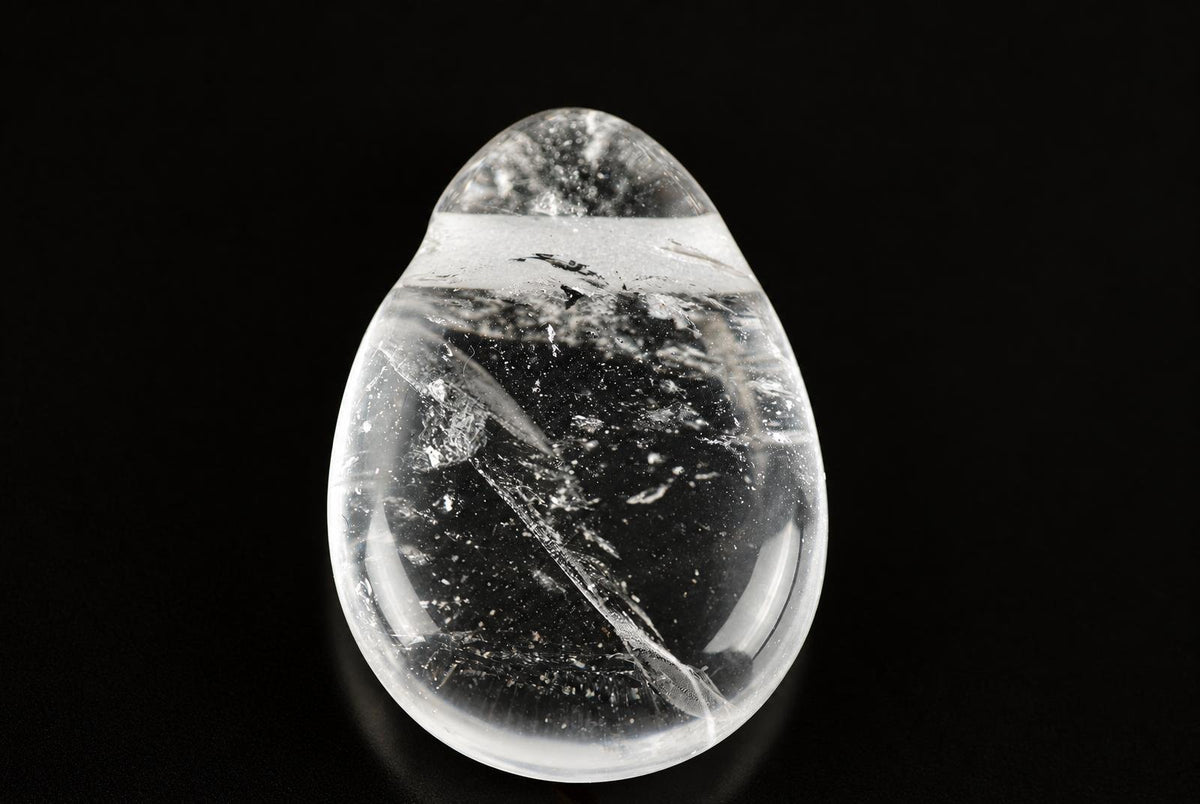 A clear quartz pendant shaped like a drop, containing dark inclusions and white streaks, set against a black background.