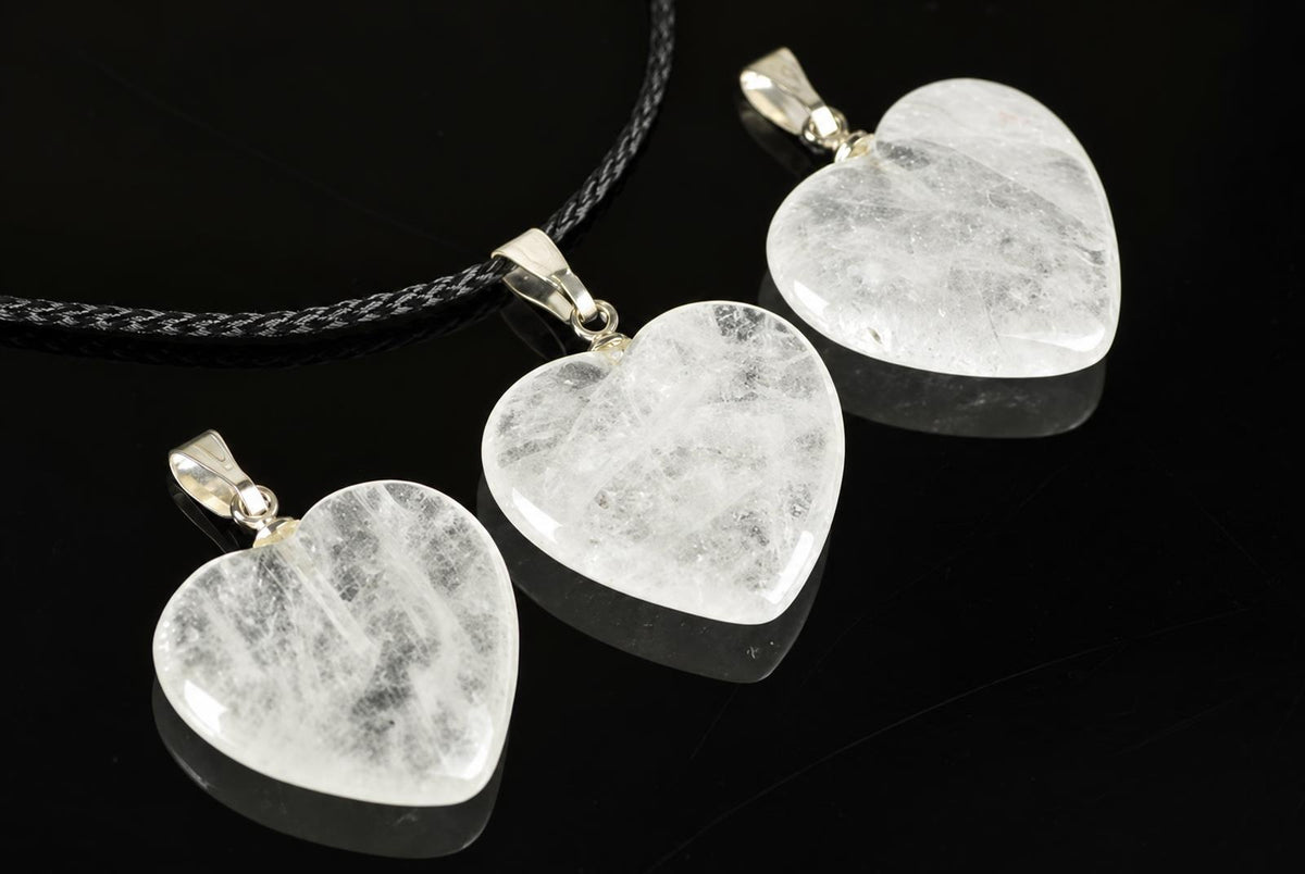 Clear quartz heart pendants with cloudy internal markings lie on a reflective black surface, with one attached to a black cord.
