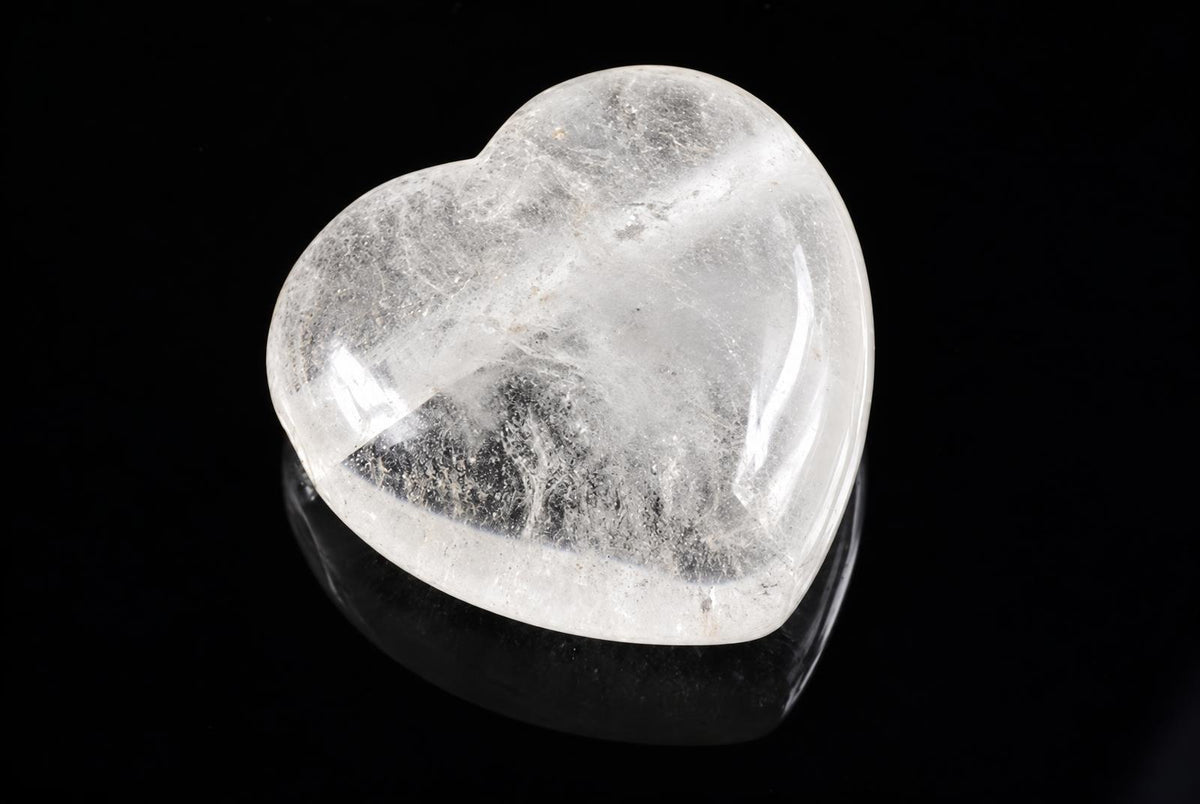 A polished, translucent white quartz heart-shaped pendant rests on a dark surface against a black background.