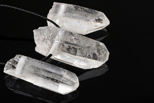 Three clear quartz crystal pendants with black cords rest on a dark, reflective surface.