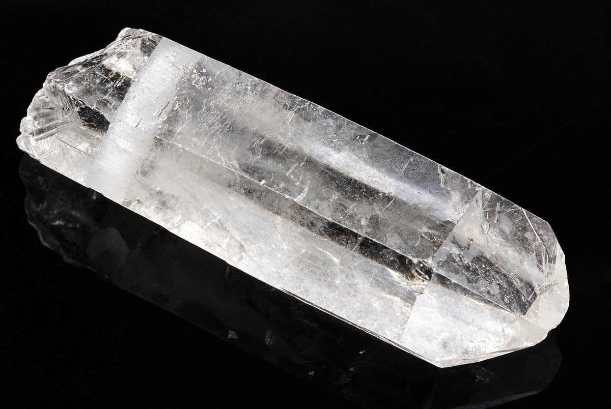 A clear quartz crystal point with a hexagonal shape, resting on a dark surface.