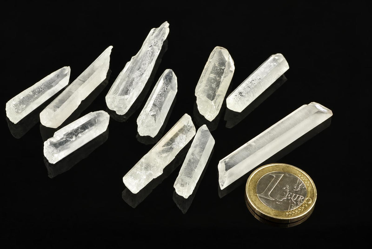 Several clear quartz points on a dark surface, with a one euro coin for scale.