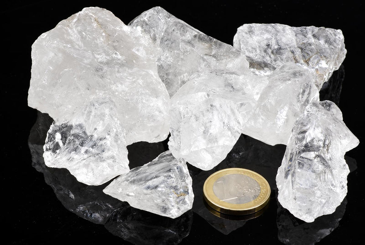 Rough clear and milky-white crystal pieces rest on a glossy black surface beside a coin.