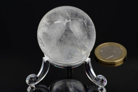 Quartz sphere – 30mm resting on a clear stand next to a coin, showcasing the natural crystal's polished and translucent surface with internal mineral inclusions.