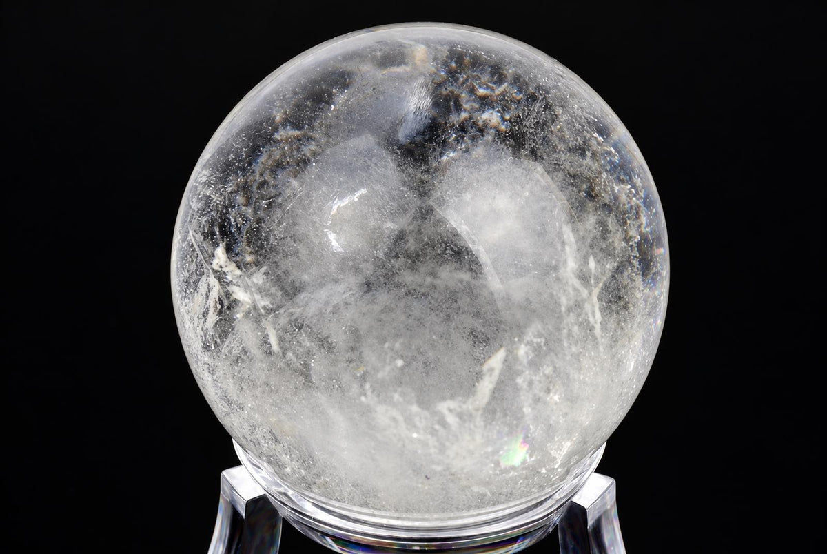 A clear quartz sphere with internal white and dark inclusions rests on a transparent stand against a black background.