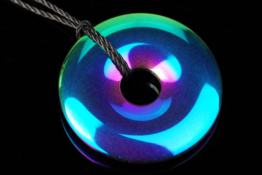 A round pendant with a rainbow iridescent finish, featuring blue, green and purple swirls on a dark surface.