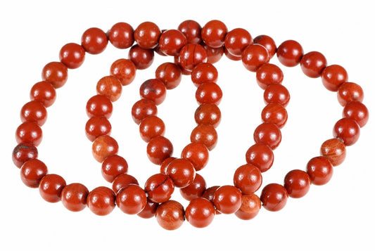 A bracelet of round, red jasper beads arranged in a coil on a white surface.