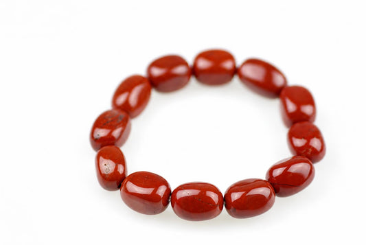 A bracelet of smooth, oval red jasper beads arranged in a circle on a pale surface.