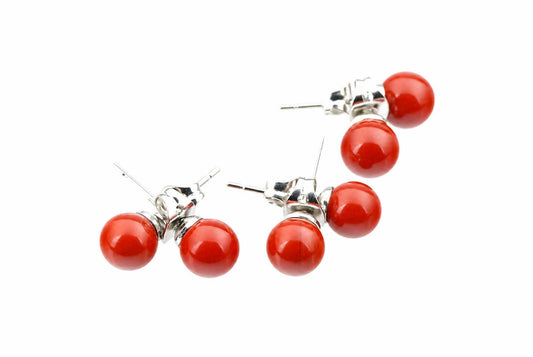 Three pairs of stud earrings with two red spherical beads each, silver-toned posts and backs on a white surface.