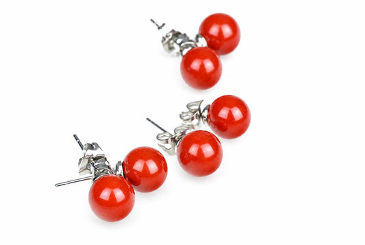 A pair of stud earrings with two red spherical beads each, set in silver-toned metal on a white surface.